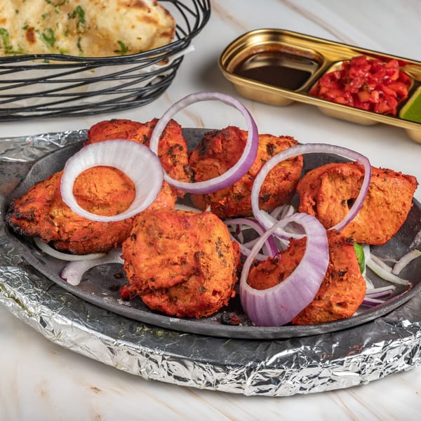 Ashoka Indian Restaurant's chicken tikka, garnished with red onion rings, served with naan and chutneys.
