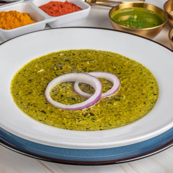 Ashoka Indian Restaurant's vibrant green Indian curry, garnished with red onion rings, alongside spices.