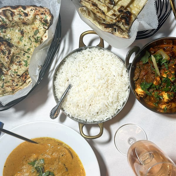 Overhead view of Ashoka Indian Restaurant's spread of naan, rice, and two curries on a white tablecloth.