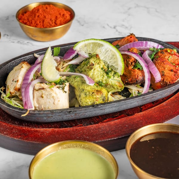 Indian chicken tikka, malai tikka, and hariyali tikka with onions and lime on a hot plate.