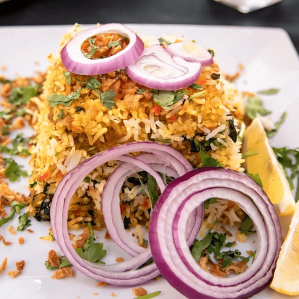 Ashoka Indian Restaurant's biryani, garnished with red onion rings, cilantro, and lemon wedges.