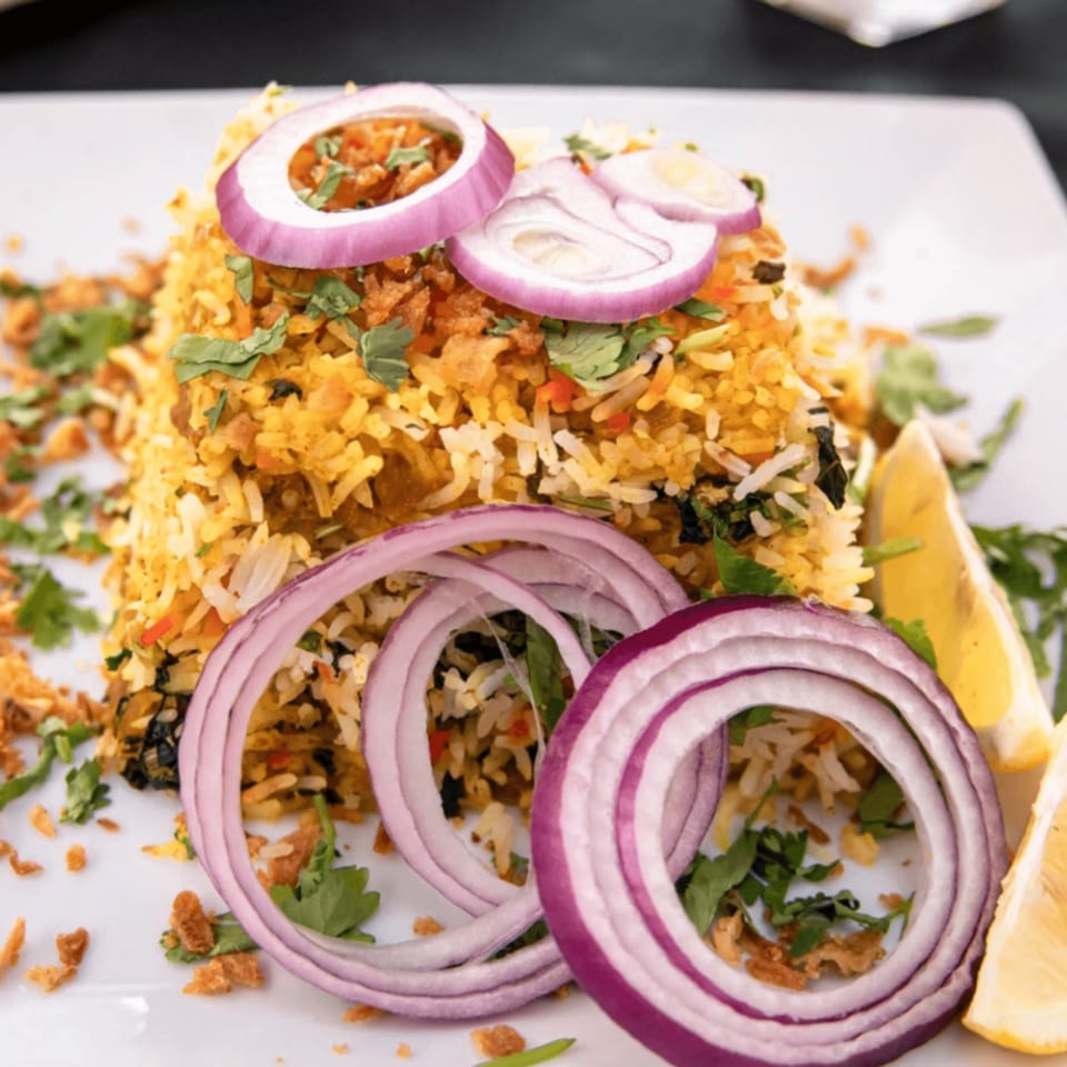 Ashoka Indian Restaurant's biryani, garnished with red onion rings, cilantro, and lemon wedges.