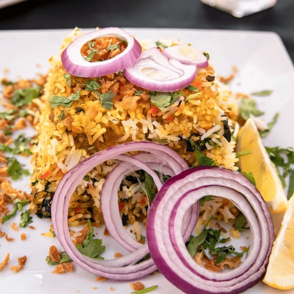 Ashoka Indian Restaurant's biryani, garnished with red onion rings, cilantro, and lemon wedges.