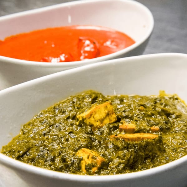 Two white bowls of Indian food, one with green palak paneer and one with orange curry.