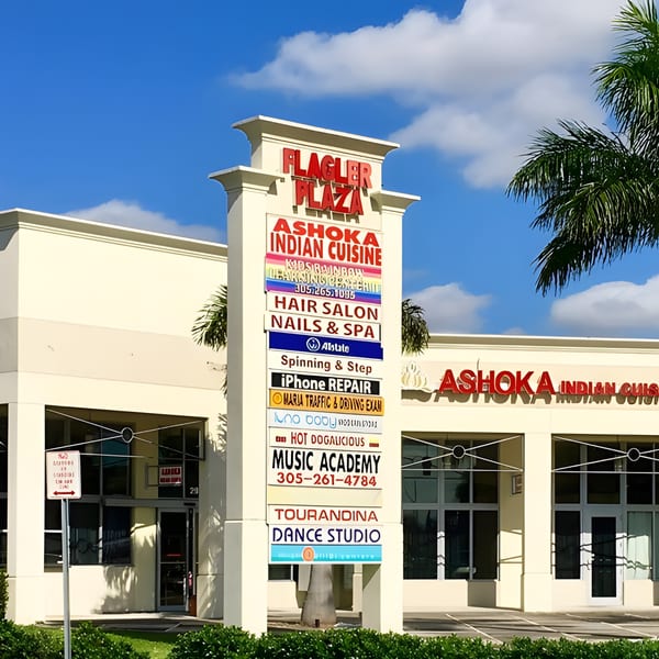 Exterior view of Flagler Plaza sign with Ashoka Indian Cuisine listed, and the restaurant's storefront.