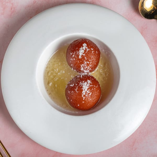 Two gulab jamun, Indian fried dough balls, in syrup with coconut flakes on a white plate.