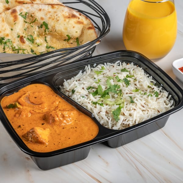 Indian takeout meal with butter chicken, rice, naan bread, and a mango lassi.