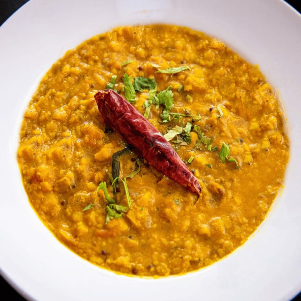 A close-up of Ashoka Indian Restaurant's yellow dal, garnished with a red chili and fresh cilantro.