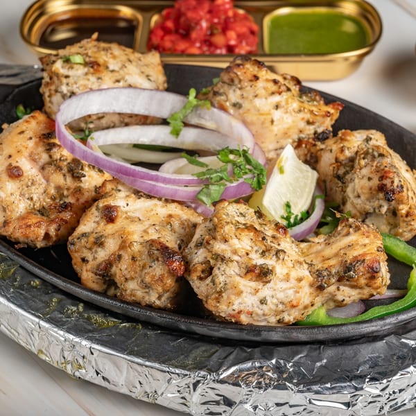 Ashoka Indian Restaurant's chicken tikka, garnished with onions, lemon, and green peppers, served with sauces.