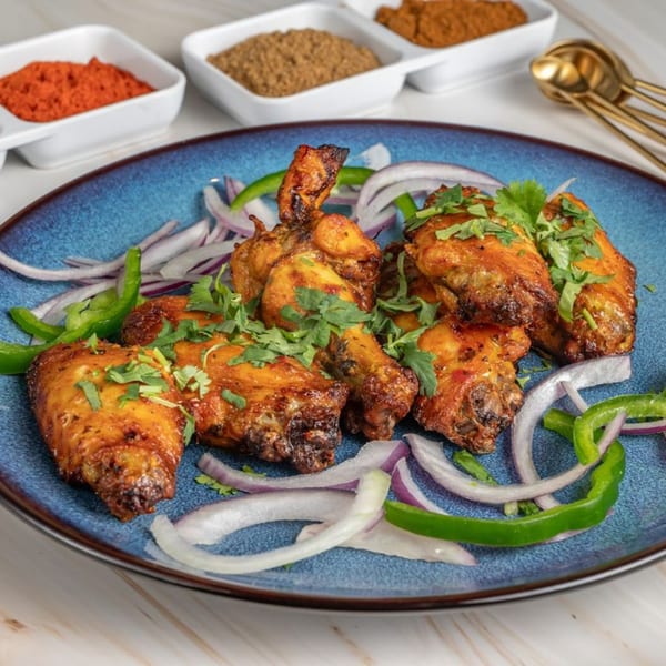 Ashoka Indian Restaurant's chicken wings on a blue plate with onions, peppers, and spices in the background.