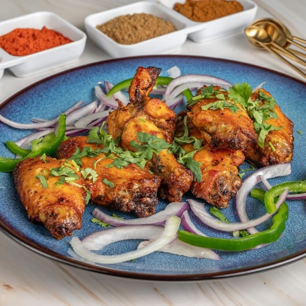 Ashoka Indian Restaurant's chicken wings, garnished with cilantro, onions, and bell peppers on a blue plate.